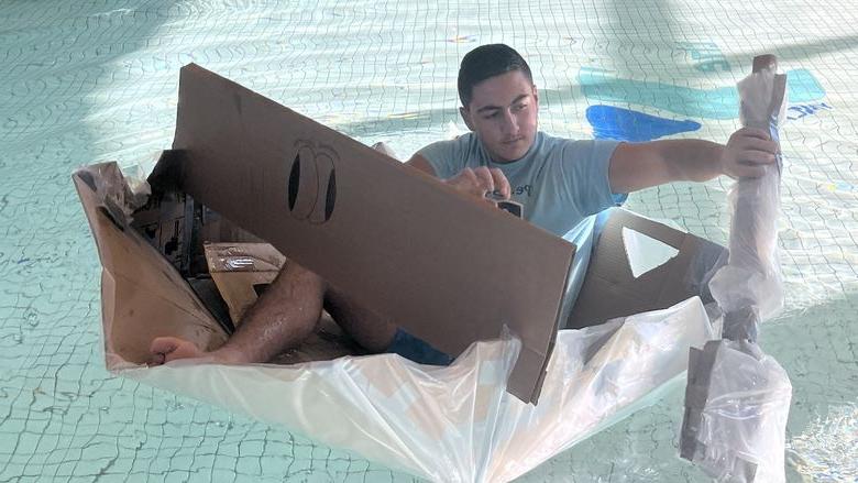 Student paddling cardboard boat in a pool